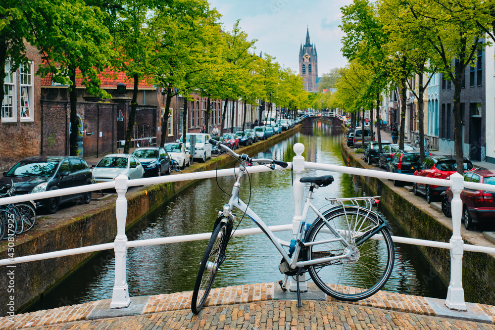 Bicycle on bridge and canal with cars parked along and Oude Kerk old church in Delft street