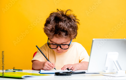 Portrait of smart school child boy at home making homework with tablet computer. Little kid in glasses with pencil writing or drawing. Elementary school and education for kindergarten kids