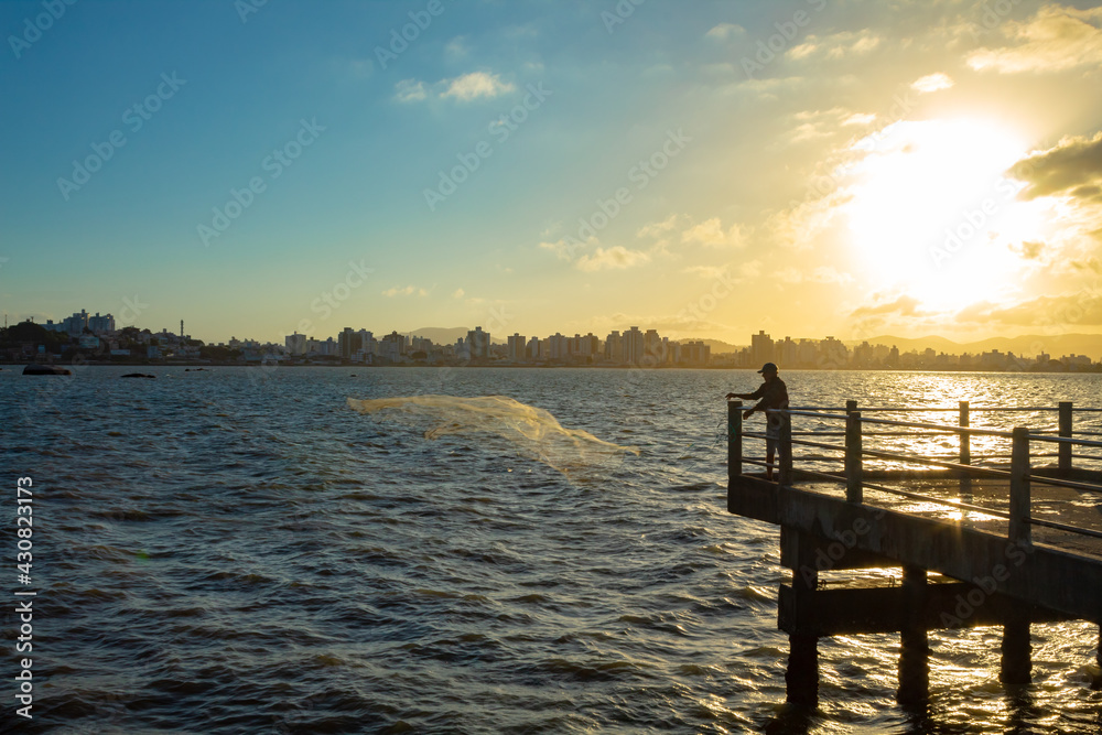 Pôr do sol e na contraluz pescador lançando uma rede no mar Florianopolis, Florianópolis, Santa Catarina, Brasil