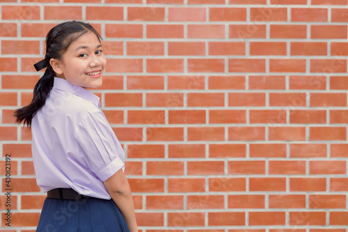 Cute girl teen student with uniform happy smile with school campus brick wall copy space.