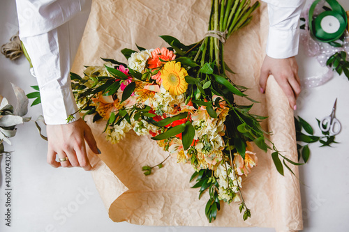 a female florist in a white shirt wraps a bouquet of fresh flowers in paper. Top view photo