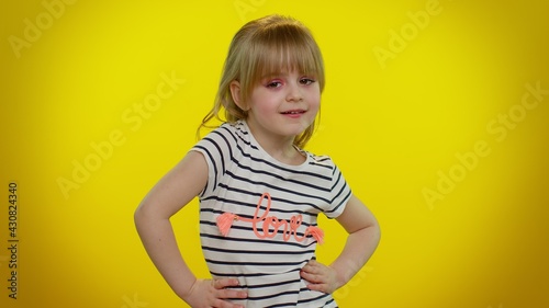 Smiling pretty little blonde teen child kid girl in white black striped t-shirt posing isolated on yellow studio background. Childhood lifestyle emotions. Young children looking at camera with smile