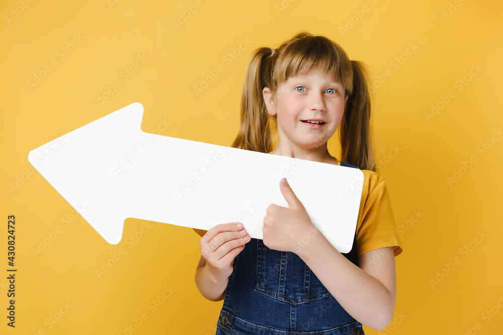 Shocked little blonde girl child wearing casual outfit standing isolated over pastel yellow studio background, pointing big white paper arrow up and showing thumb up. People emotion lifestyle concept Shocked little blonde girl child wearing casual outfit standing isolated over pastel yellow studio background, pointing big white paper arrow up and showing thumb up. People emotion lifestyle concept