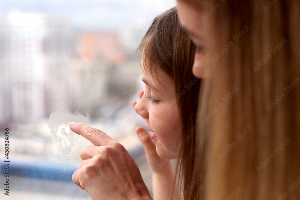 girl and mother draws heart on window. stay home at quarantine time. spend time together girl and mother draws heart on window. stay home at quarantine time. spend time together