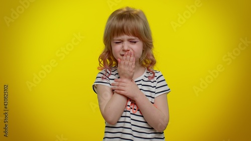 Unhealthy little blonde teen child kid girl coughing covering mouth with hand, feeling sick, allergy or viral infection symptoms. Coronavirus pandemic. Young children isolated on yellow background