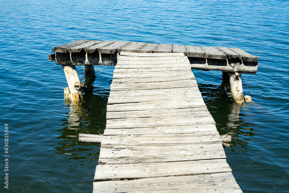 An old empty wooden deck on a lake. Fishing pier made with weathered woods.  Stock Photo