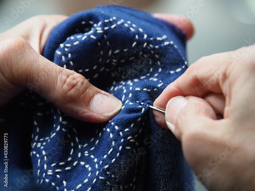 Close up needle in woman's hands sewing running stitch in blue fabric. Traditional Japanese sewing pattern call 