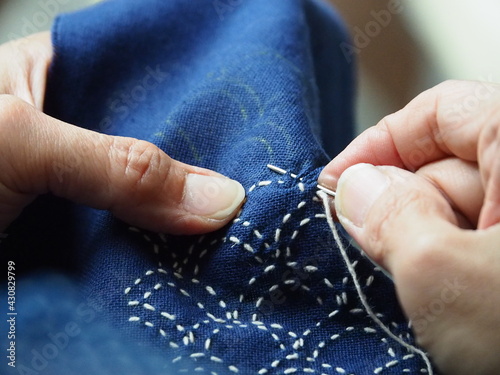 Close up needle in woman's hands sewing running stitch in blue fabric. Traditional Japanese sewing pattern call 