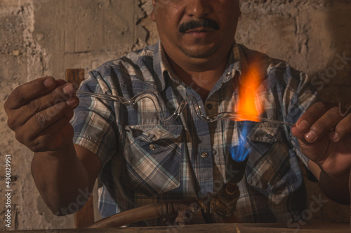 Craftsman blowing glass to create Christmas balls in his workshop, with the help of a blowtorch he shapes the glass tubes to turn them into spheres of different shapes. photo