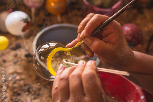 Craftsman painting Christmas spheres in his workshop in different colors, using acrylic paint, diamond paint to give texture and different figures. photo