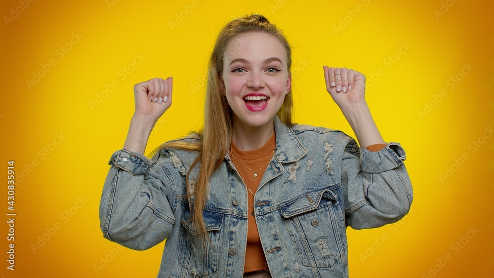 Pretty stylish teen girl in denim jacket shouting, raising fists in gesture I did it, celebrating success, winning and goal achievemen. Young adult woman indoor on yellow studio wall background Pretty stylish teen girl in denim jacket shouting, raising fists in gesture I did it, celebrating success, winning and goal achievemen. Young adult woman indoor on yellow studio wall background
