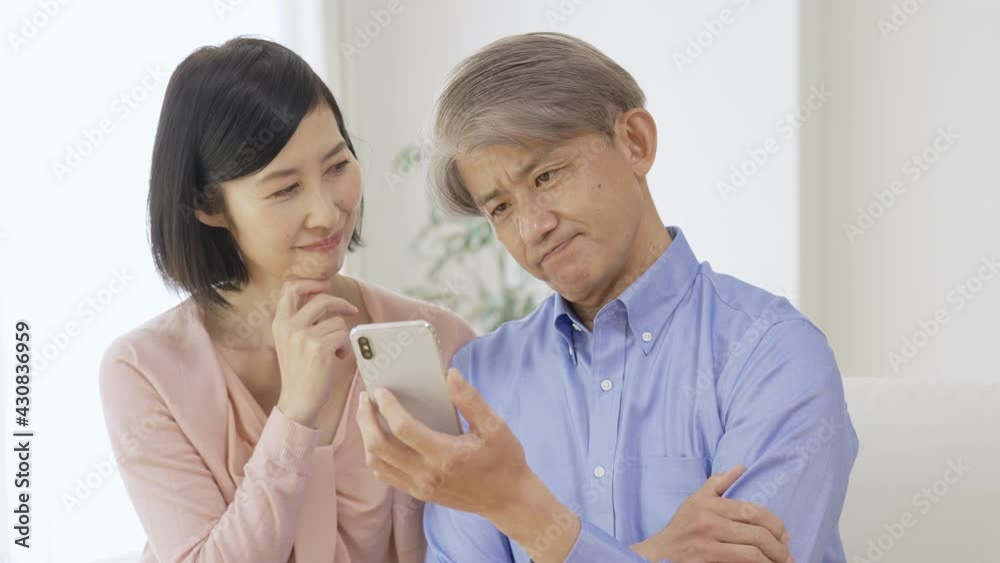 スマホを見ながら考え事をする中高年夫婦 スマホを見ながら考え事をする中高年夫婦