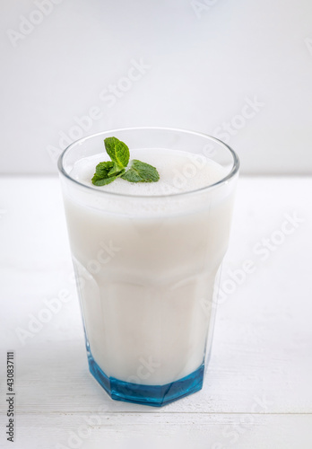 Glass of lassi Indian traditional, milky, fermented drink with mint on a light background