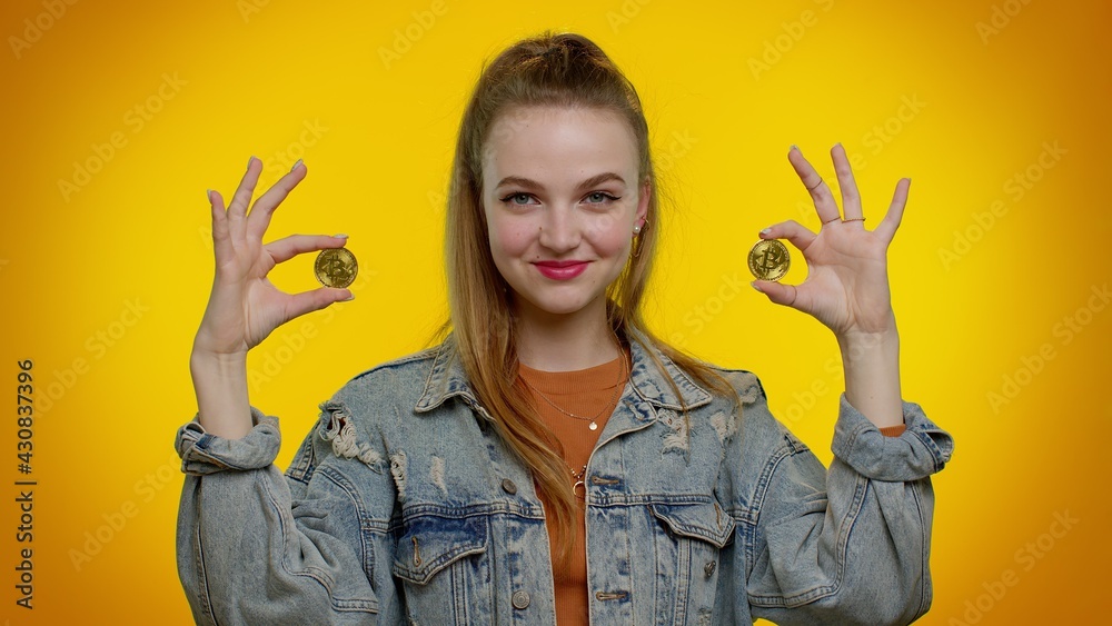 Teenager student girl in denim jacket showing golden bitcoins. Achievement career wealth, cryptocurrency investment, mining, future technology. Young fashionable woman on yellow studio background Teenager student girl in denim jacket showing golden bitcoins. Achievement career wealth, cryptocurrency investment, mining, future technology. Young fashionable woman on yellow studio background