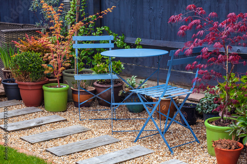 Blue bistro set in a garden surrounded by shrubs and acers