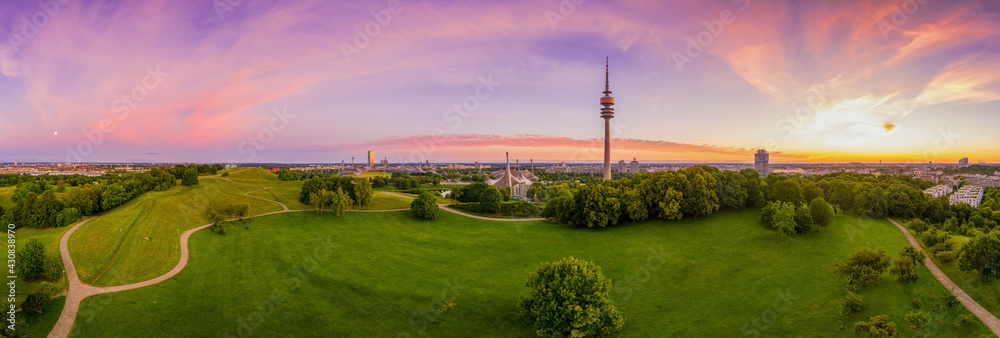 Dreamy sunrise over Munichs popular Olympic Park from a high and panoramic view with a violet morning sky over the sightseeing idyllic hotspot in the center of the bavarian capital.
