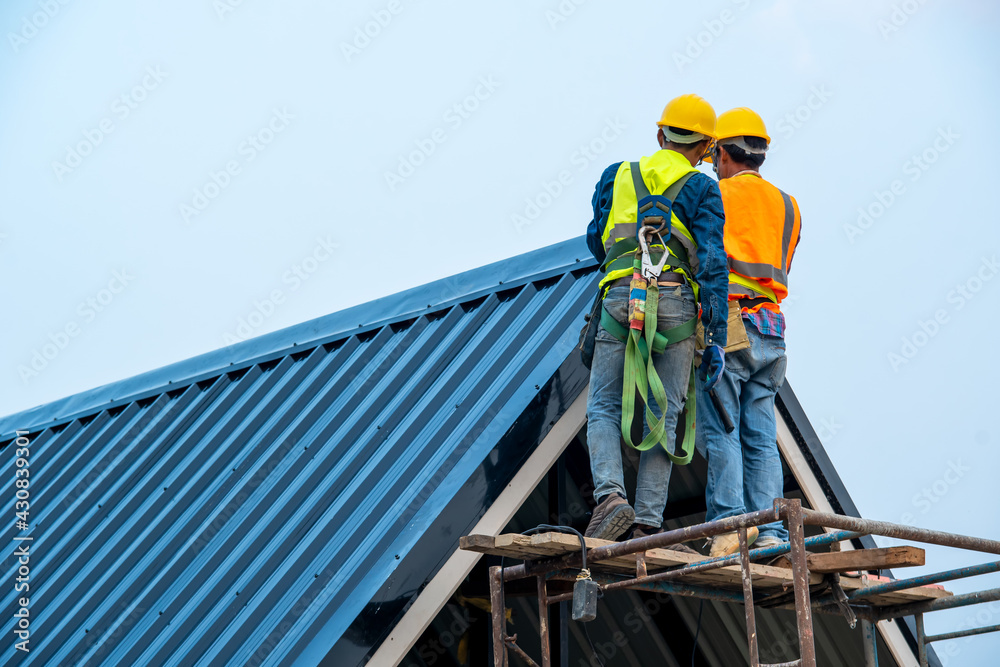 Roofer worker in protective uniform wear and gloves,Roofing tools,installing new roofs under construction,Electric drill used on new roofs with metal sheet. Roofer worker in protective uniform wear and gloves,Roofing tools,installing new roofs under construction,Electric drill used on new roofs with metal sheet.