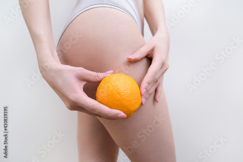 young woman is holding an orange on a light background.