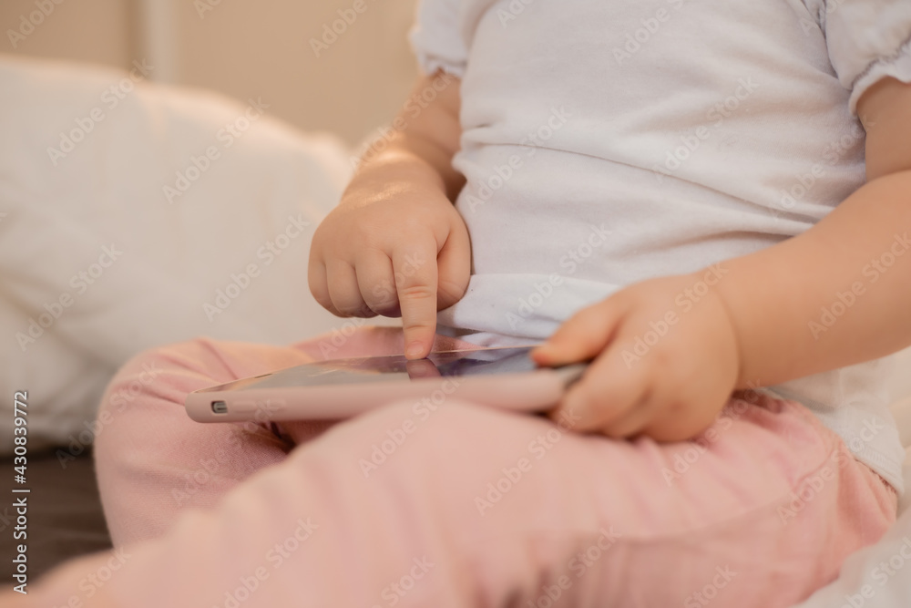 Baby blonde girl plays with the phone at home on the bed. Children and technology