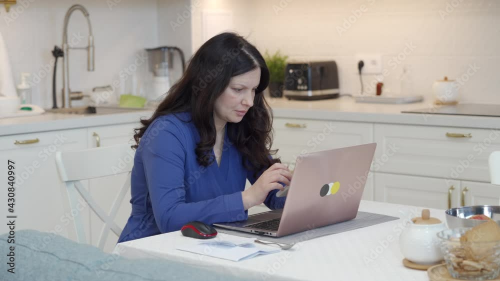 Woman working with laptop computer in the kitchen at home, white kitchen interior of modern apartment. High quality 4k footage Woman working with laptop computer in the kitchen at home, white kitchen interior of modern apartment. High quality 4k footage