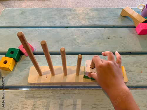 Toddler is playing Wooden puzzle stacking tower. Children's educational toys. Block ring toss puzzle. Wooden puzzle stacking tower. The toddler's hand is playing to enter the block into the stick