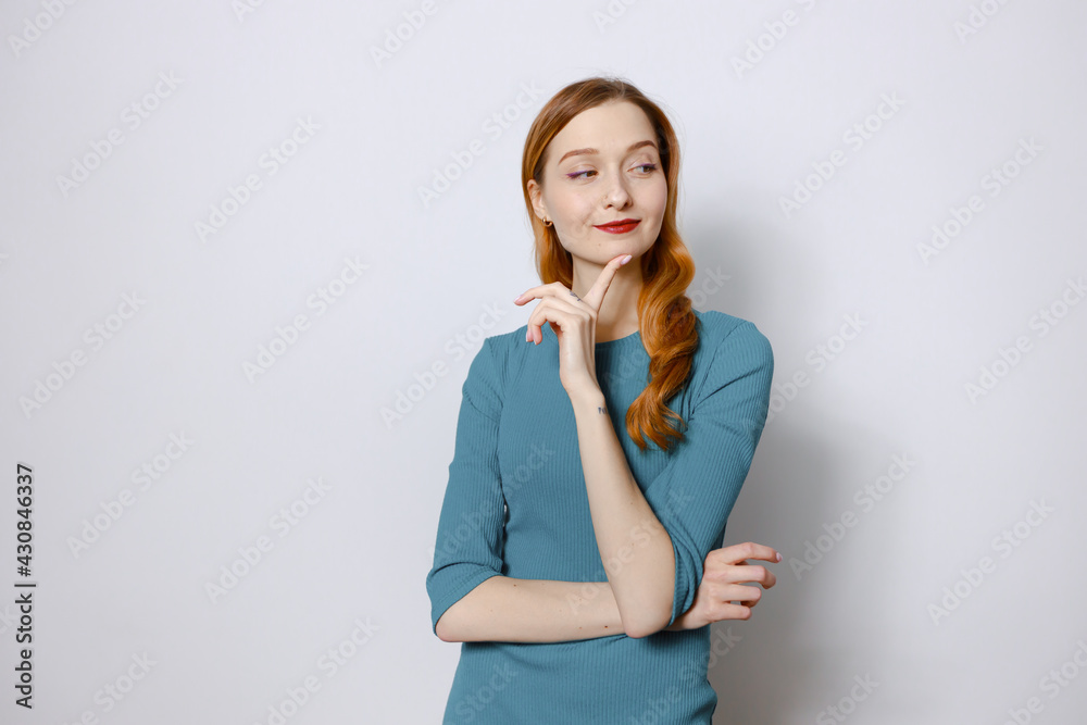 Portrait of a cheerful, thoughtful red-haired woman in a blue dress on a white background. Copy space. Portrait of a cheerful, thoughtful red-haired woman in a blue dress on a white background. Copy space.