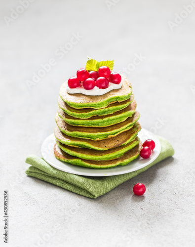 Green spinach pancakes with matcha tea with cranberries on a plate on a light gray background