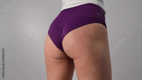 Close-up of a woman in shorts slaps herself on the ass on a white background in the studio