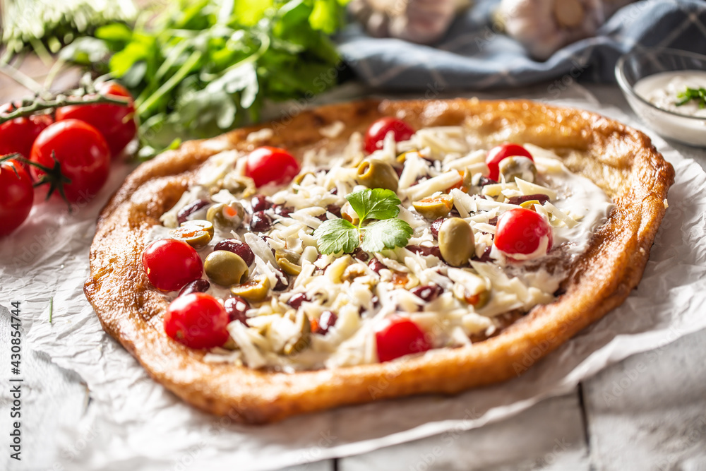 Tasty and crusty langos perfectly served with whole cherry tomatoes, gratted cheese, beans and green greek olives