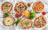 A close up a set of hungarian traditional langos with crusty garlic edges served with vegetables, cream sausages, herbs, grated, cheese, ketchup and dips and oil
