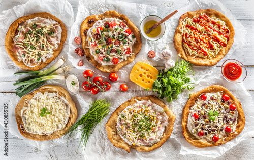 A close up a set of hungarian traditional langos with crusty garlic edges served with vegetables, cream sausages, herbs, grated, cheese, ketchup and dips and oil