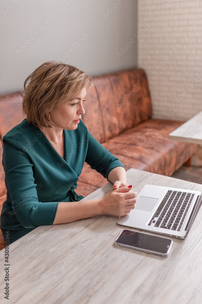 An adult female psychologist coach conducts an online consultation in the bright interior of a cafe with a laptop and a phone on the table. the concept of remote work and psychological assistance. An adult female psychologist coach conducts an online consultation in the bright interior of a cafe with a laptop and a phone on the table. the concept of remote work and psychological assistance.