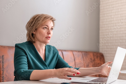 An adult female psychologist coach conducts an online consultation in the bright interior of a cafe with a laptop and a phone on the table. the concept of remote work and psychological assistance.