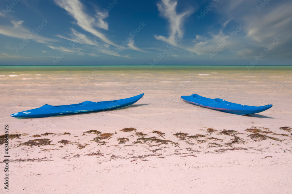 Two kaiaks on a deserted tropical beach on Holbox Island in Mexico. In the background the Caribbean sea and the sky partially cloudy. Ideal place for vacations Two kaiaks on a deserted tropical beach on Holbox Island in Mexico. In the background the Caribbean sea and the sky partially cloudy. Ideal place for vacations