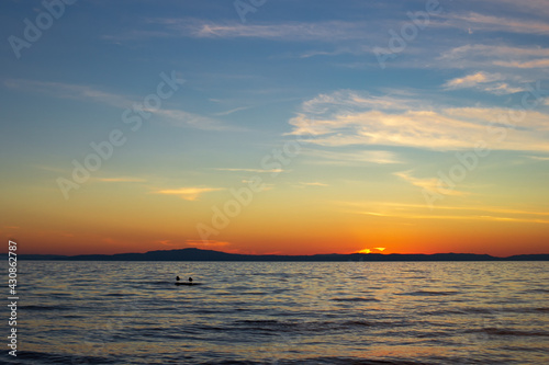 Scenic sunset on lake in dusk with blue clear sky and cirrus clouds, gulls on stone in calm waves under sundown blazing © Clara_Sh.