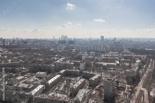Aerial view of residential areas of a large city with multi-storey buildings against a blue sky with light clouds in early spring with snow on the ground and trees without foliage © Igor