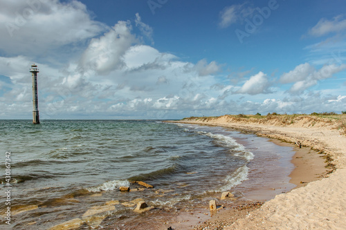 Sunny summer day by Baltic Sea.Wandelust Travel background.Power of water energy passing.Amazing view of cold sea with old lighthouse, waves and pebble sandy beach.Coastline of Estonia.