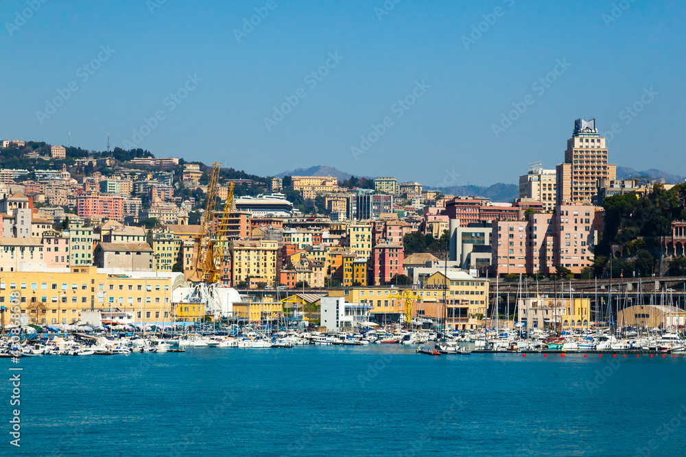 Scenic view of the maritime city of Genoa in Italy. View from the sea to the Italian city of Genoa, beautiful colorful houses along the coast, harbor cranes and yachts moored at the pier.