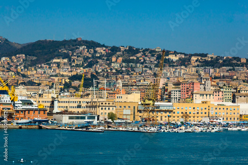 Scenic view of the maritime city of Genoa in Italy. View from the sea to the Italian city of Genoa, beautiful colorful houses along the coast, harbor cranes and yachts moored at the pier.