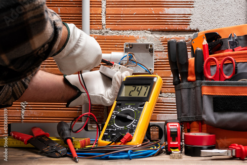Electrician worker at work with the tester measures the voltage in an electrical system. Working safely with protective gloves. Construction industry.