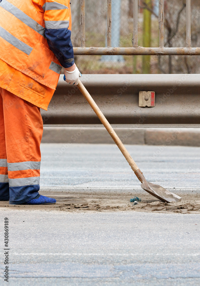 The janitor scrapes the accumulated sand between the lanes of the road under the metal bumper with a shovel. The janitor scrapes the accumulated sand between the lanes of the road under the metal bumper with a shovel.