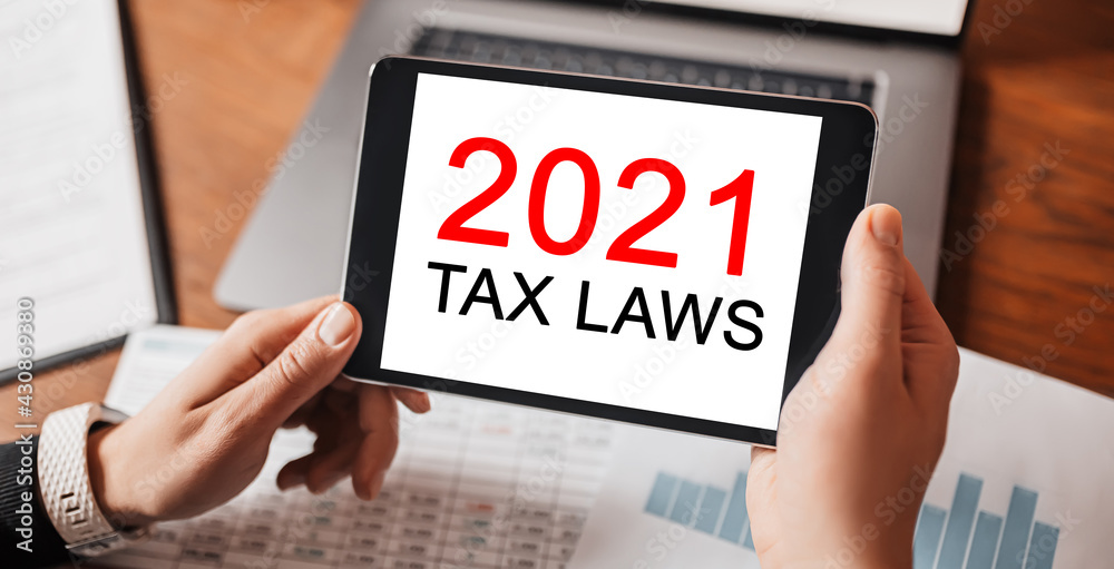 Man hands holding tablet with text 2021 tax laws at workplace. Businessman working at desk with documents Man hands holding tablet with text 2021 tax laws at workplace. Businessman working at desk with documents