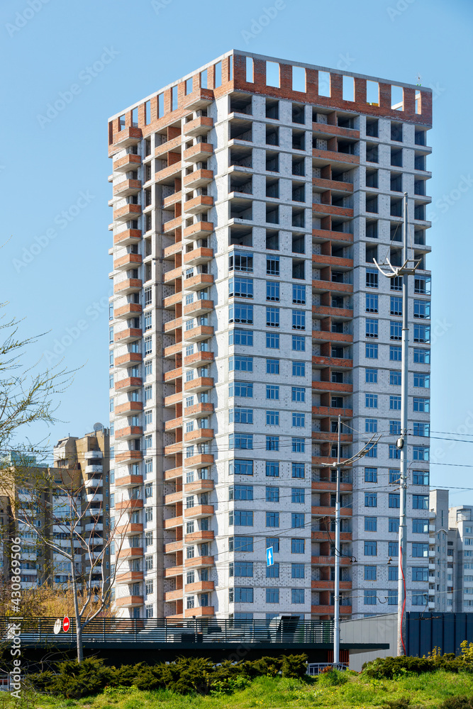 Construction of a new multi-storey residential building with a square-shaped building against a background of blue sky and green lawn on a bright day. Construction of a new multi-storey residential building with a square-shaped building against a background of blue sky and green lawn on a bright day.