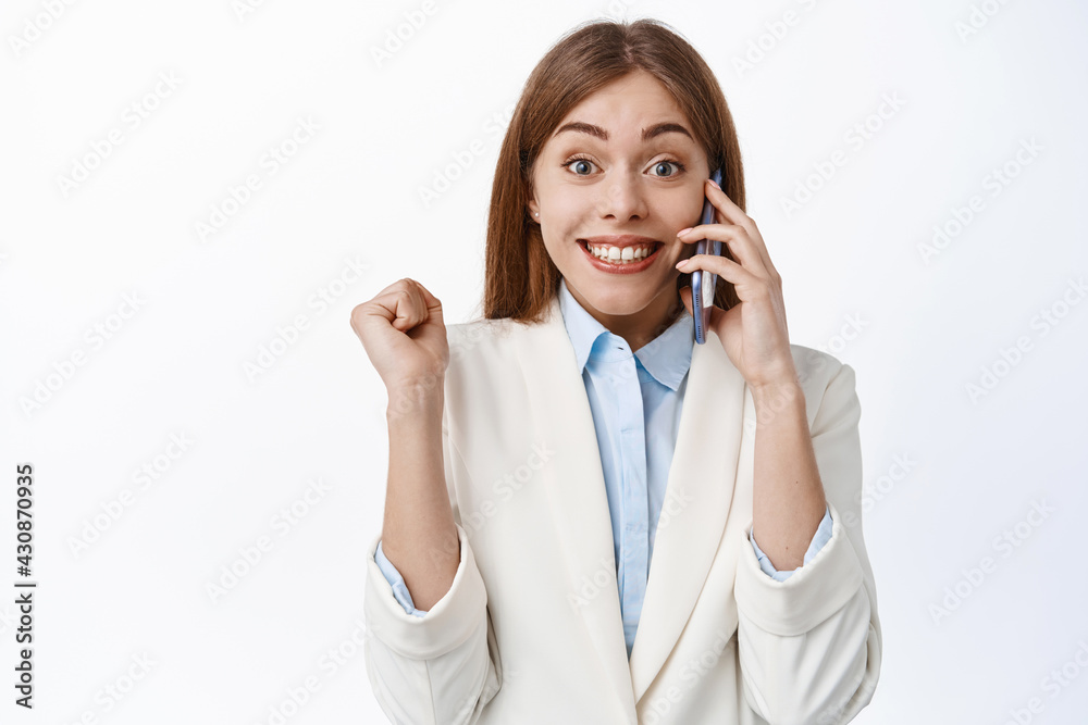Happy office woman, elegant lady in white suit answer phone call and jump from happiness, receive great news, winning and celebrating, standing over white background Happy office woman, elegant lady in white suit answer phone call and jump from happiness, receive great news, winning and celebrating, standing over white background