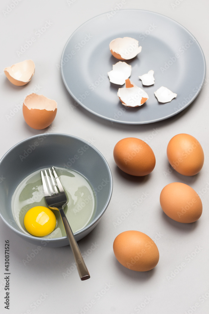 Broken egg and fork in gray bowl. Chicken shells on gray plate. Brown eggs on table Broken egg and fork in gray bowl. Chicken shells on gray plate. Brown eggs on table