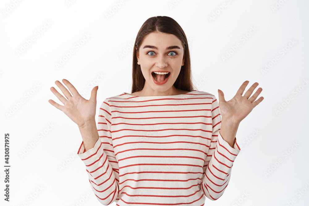 Portrait of young woman shouting from surprise and happiness, smiling, reacting on good awesome news, spread hands sideways, happy for you, standing over white background Portrait of young woman shouting from surprise and happiness, smiling, reacting on good awesome news, spread hands sideways, happy for you, standing over white background