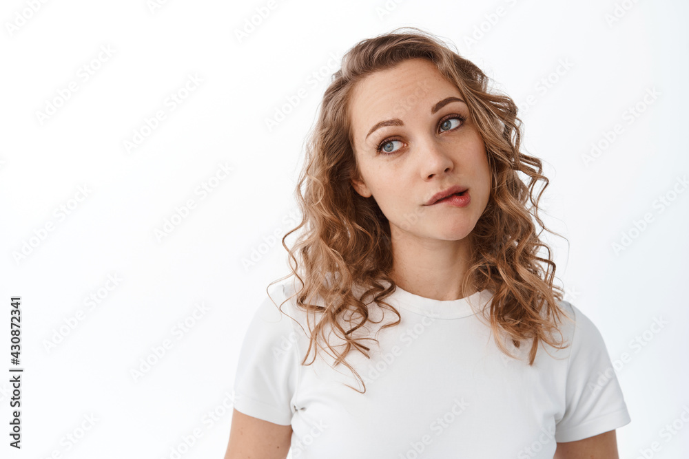 Cute silly woman biting lip and look thoughtful aside, dreaming or wanting something, daydreaming, standing over white background Cute silly woman biting lip and look thoughtful aside, dreaming or wanting something, daydreaming, standing over white background