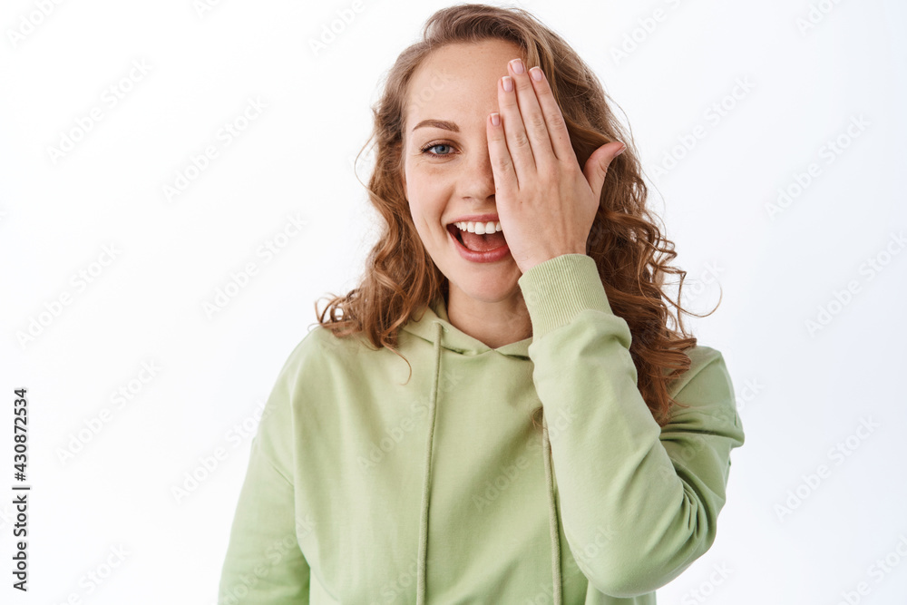 Happy attractive woman cover half of face with hand and smile, showing before after effect, hiding eye behind palm, standing over white background Happy attractive woman cover half of face with hand and smile, showing before after effect, hiding eye behind palm, standing over white background