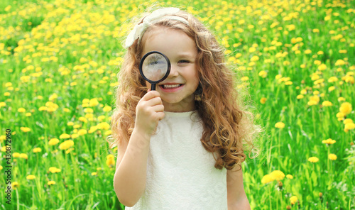 Child looking through a magnifying glass on the grass in summer day