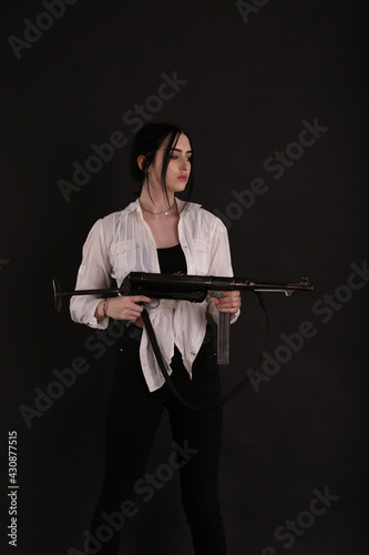 Brunette woman in white shirt with submachine gun in her hands on black background